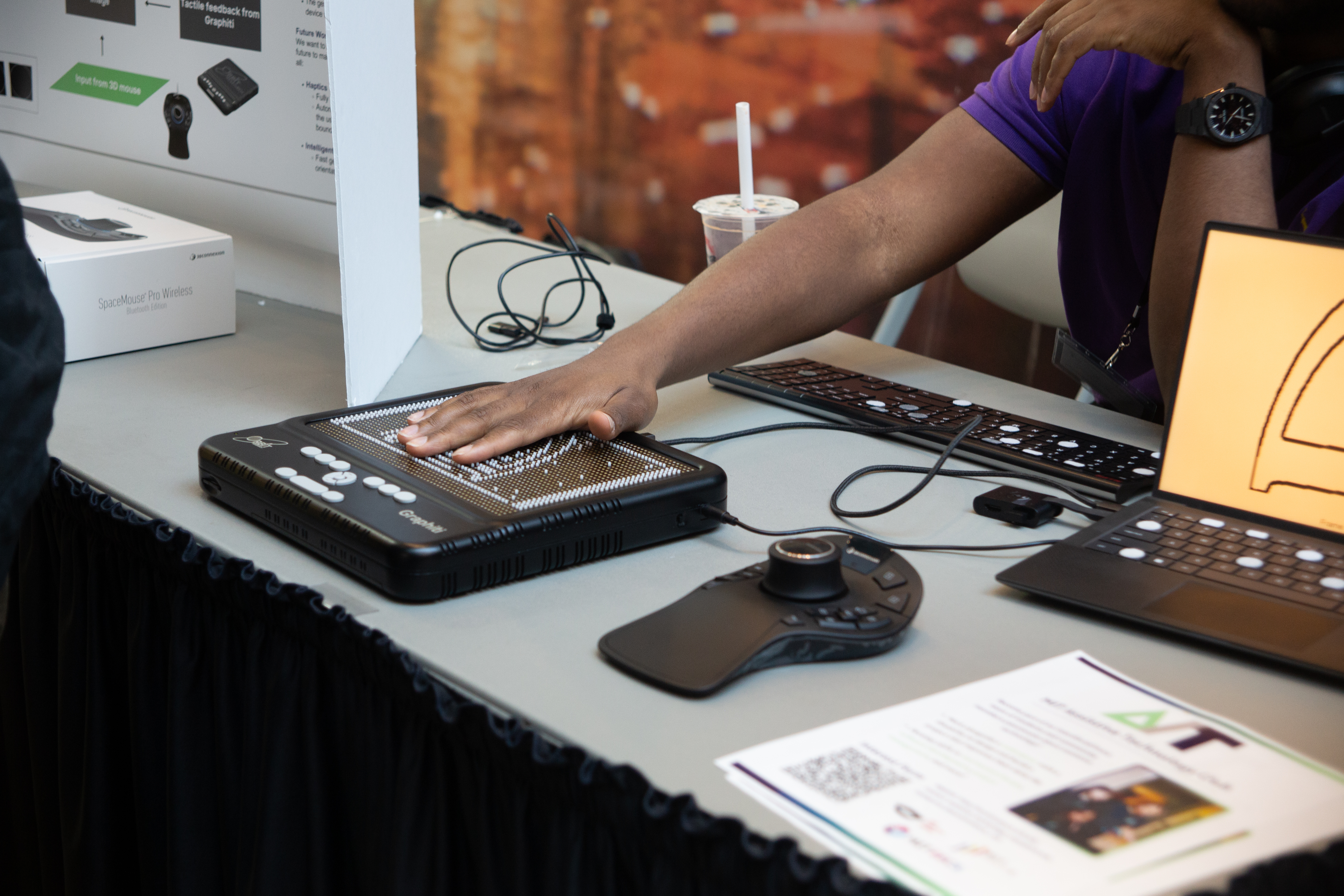 A hand reaches out to feel a tactile board (Graphiti) that displays the cross-section of a 3D CAD model.